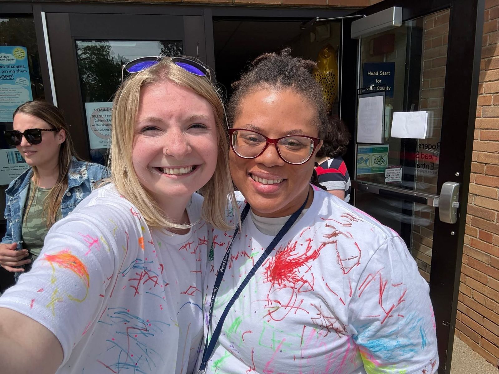 Two women in paint-splattered shirts smiling